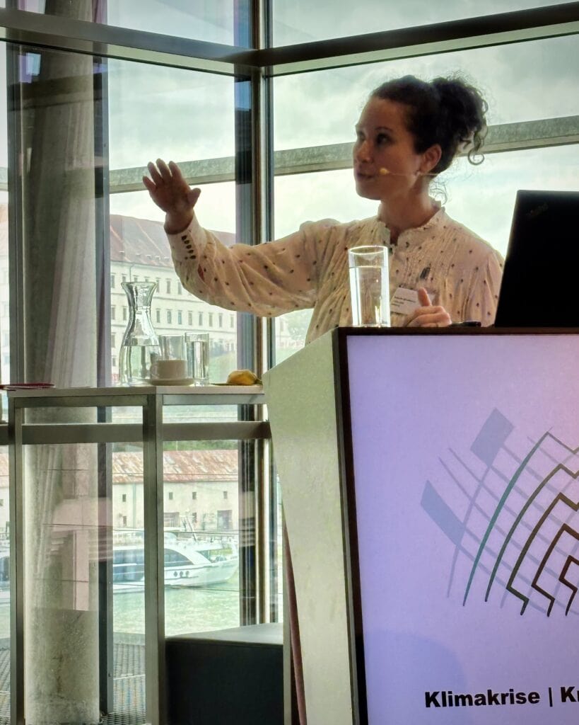 Innovative Frau bei Vortrag über Klimakrise und Nachhaltigkeit im Konferenzraum, engagiert und professionell, mit Präsentation und Wasser im Hintergrund.