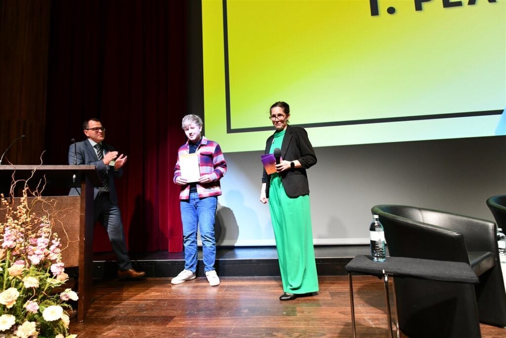 Hochwertiges Foto einer Preisverleihung der Richtervereinigung bei einer Veranstaltung, mit einer jungen Preisträgerin und Moderatorinnen auf der Bühne, professionell und ansprechend inszeniert.